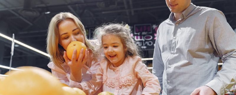 Family enjoying a cheerful shopping trip together at the grocery store, selecting fresh oranges.